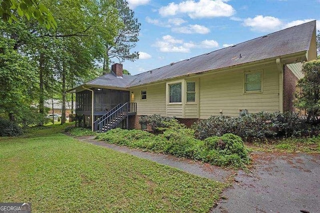 rear view of property with a chimney, a sunroom, and a lawn