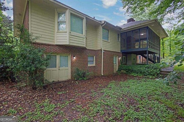 rear view of house with stairway, a chimney, brick siding, and a sunroom