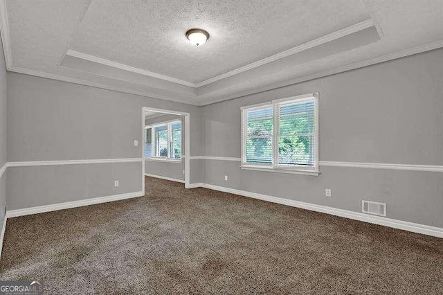 spare room featuring a tray ceiling, crown molding, visible vents, dark carpet, and a textured ceiling