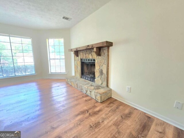 5229 Mountain Village Ct, Stone Mountain, GA 30083 - unfurnished living room featuring a textured ceiling, visible vents, baseboards, a fireplace, and wood finished floors