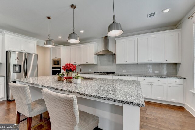 kitchen with appliances with stainless steel finishes, wall chimney range hood, white cabinets, a sink, and visible vents
