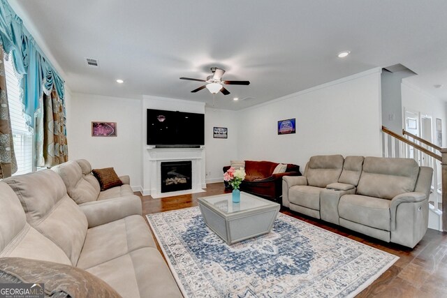 living area featuring visible vents, ornamental molding, a ceiling fan, and dark wood-type flooring