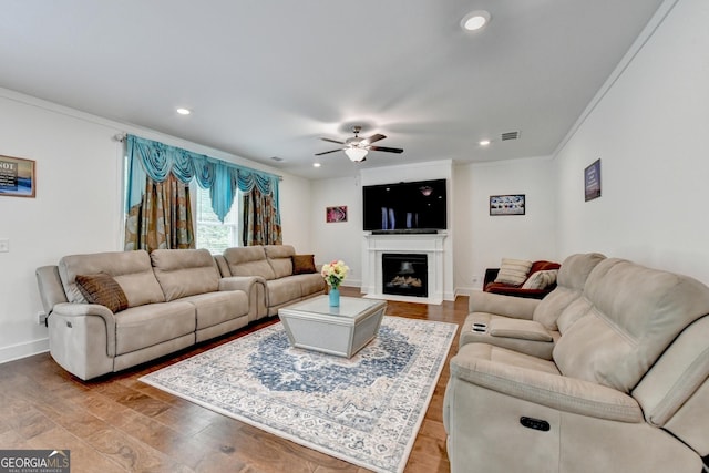 living room featuring recessed lighting, light wood-type flooring, a ceiling fan, visible vents, and ornamental molding