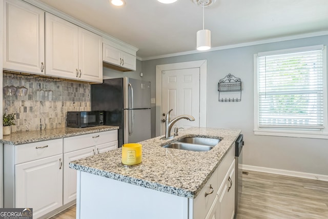 kitchen with a sink, black microwave, freestanding refrigerator, a kitchen island with sink, and backsplash