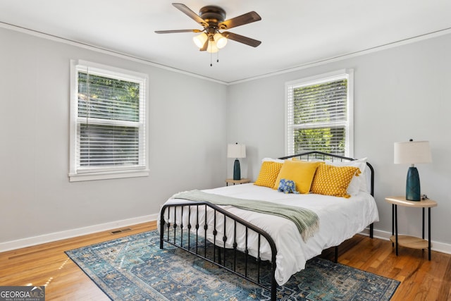 bedroom with baseboards, wood finished floors, ornamental molding, and multiple windows