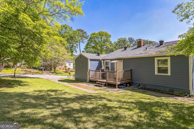 rear view of property with a deck, a yard, roof with shingles, and a chimney