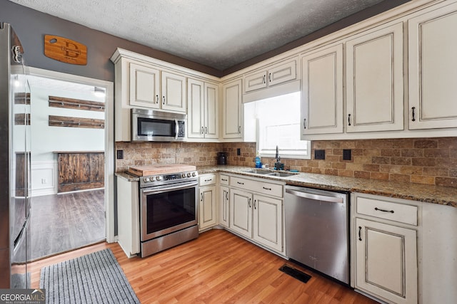 kitchen with a sink, light wood finished floors, appliances with stainless steel finishes, and cream cabinetry