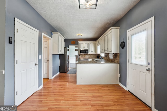kitchen featuring a textured ceiling, light wood-type flooring, a sink, a peninsula, and stainless steel appliances