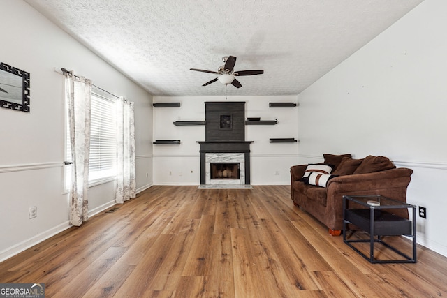 living room with ceiling fan, a textured ceiling, wood finished floors, baseboards, and a premium fireplace