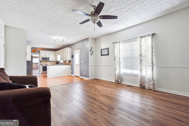 living room with a textured ceiling, baseboards, a ceiling fan, and light wood-style flooring