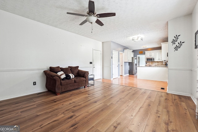 living area with baseboards, a ceiling fan, light wood-type flooring, and a textured ceiling