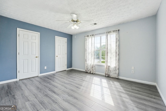unfurnished bedroom with a textured ceiling, baseboards, wood finished floors, and visible vents