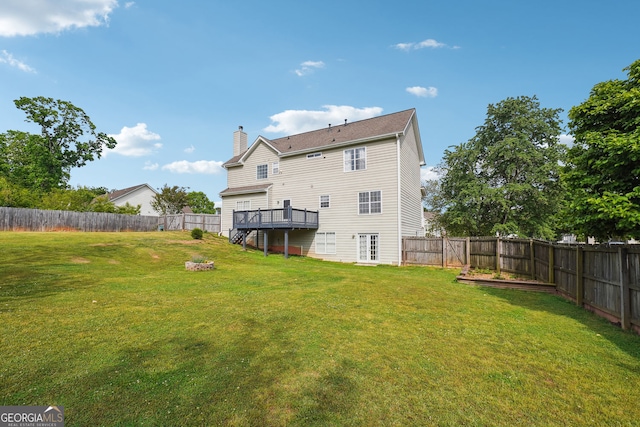 back of property with a fenced backyard, a wooden deck, a chimney, and a lawn