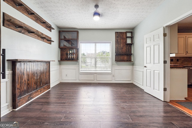 unfurnished dining area featuring a textured ceiling, dark wood-style floors, and a wainscoted wall