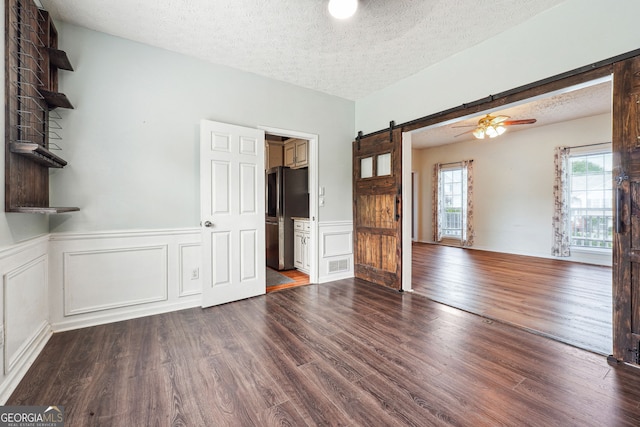unfurnished living room featuring a barn door, a textured ceiling, and dark wood-style floors