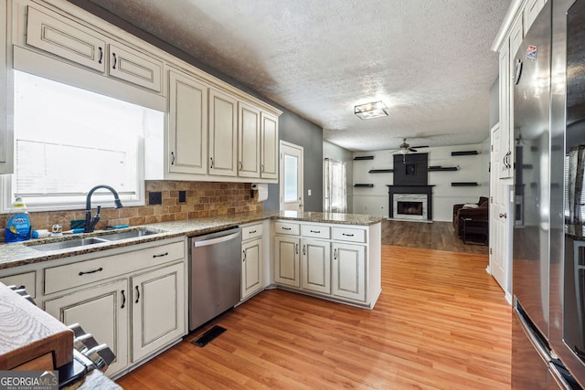 kitchen with light wood-type flooring, a sink, a peninsula, open floor plan, and stainless steel appliances