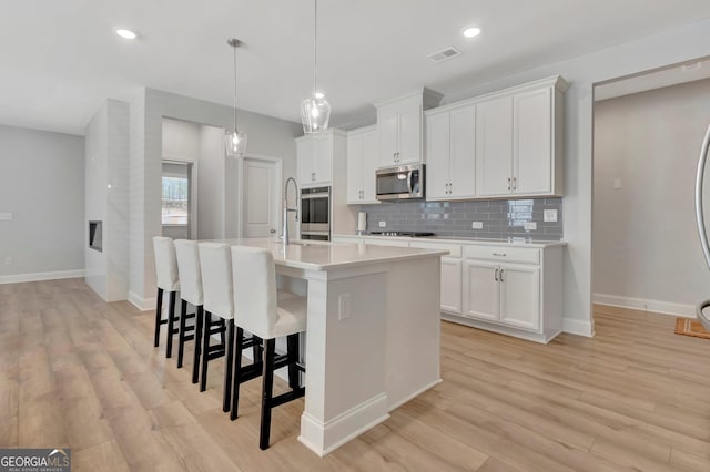kitchen featuring visible vents, stainless steel appliances, baseboards, an island with sink, and backsplash