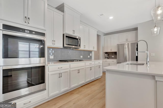 kitchen featuring appliances with stainless steel finishes, white cabinetry, light wood-style floors, and a sink