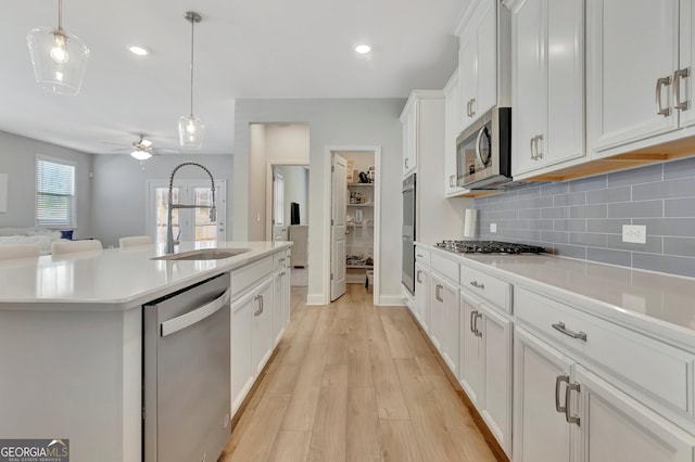 kitchen featuring appliances with stainless steel finishes, light countertops, backsplash, a sink, and white cabinetry