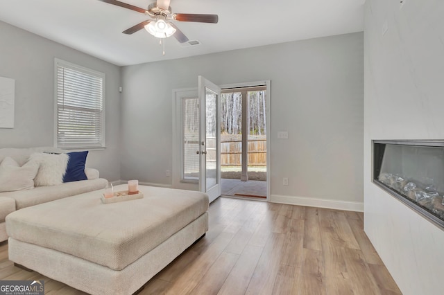 interior space featuring visible vents, light wood-style floors, baseboards, a ceiling fan, and access to outside
