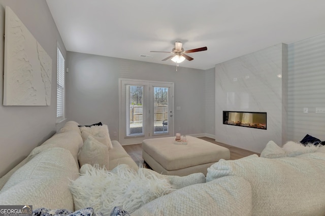 living area with a high end fireplace, a ceiling fan, visible vents, and wood finished floors