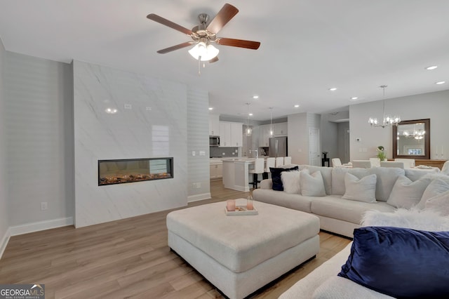 living area featuring recessed lighting, light wood-style flooring, baseboards, and ceiling fan with notable chandelier