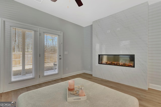 interior space with baseboards, wood finished floors, a ceiling fan, and a glass covered fireplace