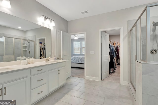 full bath with a sink, a shower stall, ceiling fan, double vanity, and visible vents