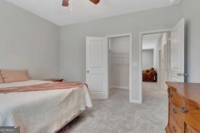 bedroom featuring a closet, a ceiling fan, a walk in closet, baseboards, and light colored carpet