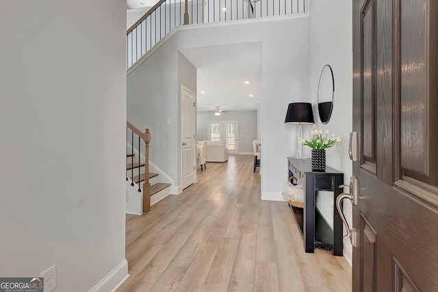 foyer featuring stairs, light wood-style floors, baseboards, a ceiling fan, and a towering ceiling