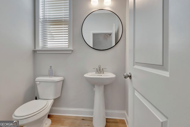 half bathroom with wood finished floors, toilet, and baseboards