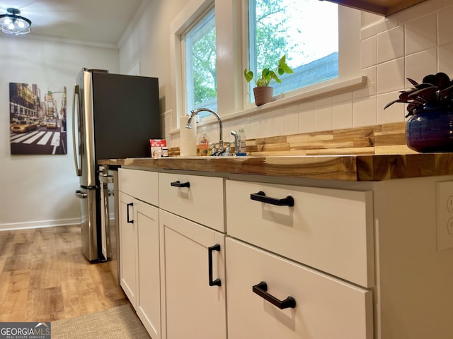 kitchen featuring freestanding refrigerator, white cabinetry, decorative backsplash, and light wood-style floors