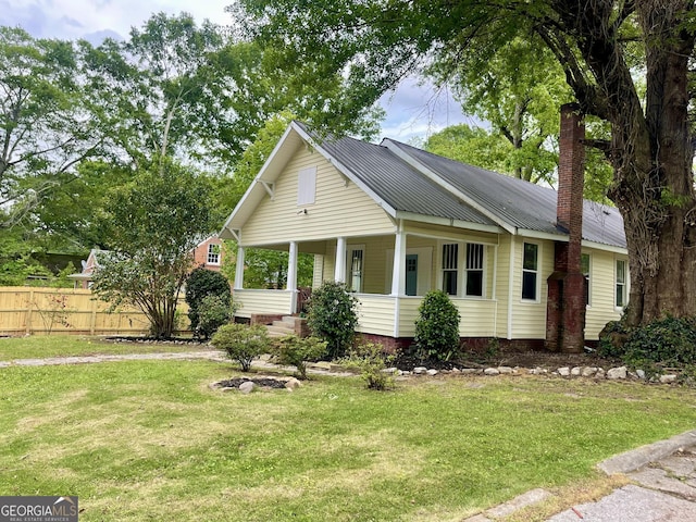 bungalow featuring a chimney, metal roof, fence, a porch, and a front lawn