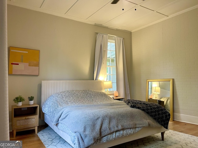 bedroom with wood finished floors and brick wall