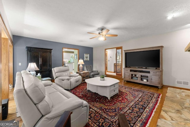 living area with a textured ceiling, visible vents, baseboards, wood finished floors, and a ceiling fan