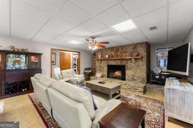 tiled living area featuring a paneled ceiling, visible vents, a stone fireplace, and a ceiling fan