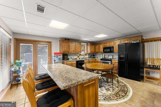kitchen featuring light tile patterned floors, light countertops, black appliances, visible vents, and a paneled ceiling