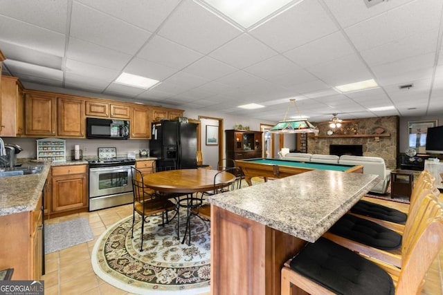 kitchen featuring brown cabinetry, black appliances, a sink, a kitchen breakfast bar, and a paneled ceiling