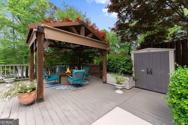 wooden deck with a fire pit, a gazebo, a storage shed, and an outbuilding