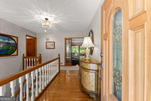 hall featuring an upstairs landing, a notable chandelier, and wood finished floors