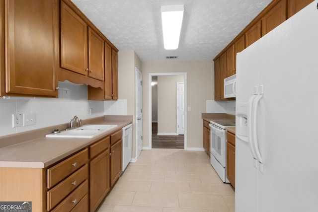 kitchen featuring white appliances, brown cabinetry, light countertops, a sink, and visible vents