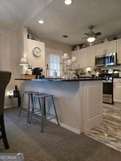 kitchen with appliances with stainless steel finishes, a breakfast bar, white cabinets, ceiling fan, and dark countertops