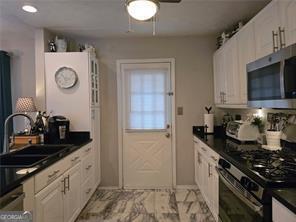 6193 Charring Cross Ct, Lithonia, GA 30058 - kitchen featuring stainless steel microwave, gas range oven, a sink, dark countertops, and white cabinetry