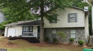 tri-level home with covered porch, a garage, and stone siding