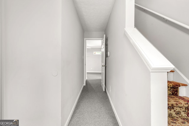 hallway with a textured ceiling, carpet flooring, and baseboards