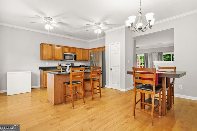 kitchen with light wood-style floors, a kitchen breakfast bar, dark countertops, appliances with stainless steel finishes, and ceiling fan with notable chandelier