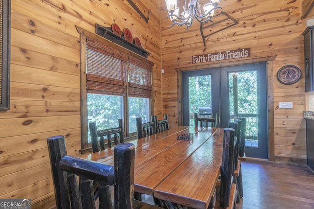 dining area with wooden walls, a notable chandelier, wood finished floors, and french doors