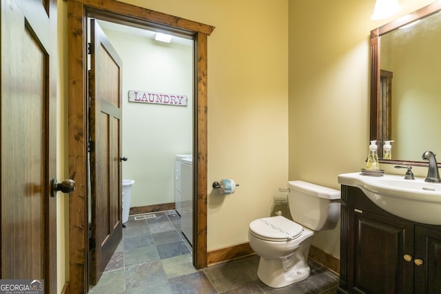 bathroom featuring vanity, separate washer and dryer, toilet, stone finish floor, and baseboards