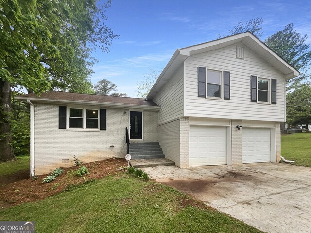 tri-level home with concrete driveway, an attached garage, a front lawn, and brick siding