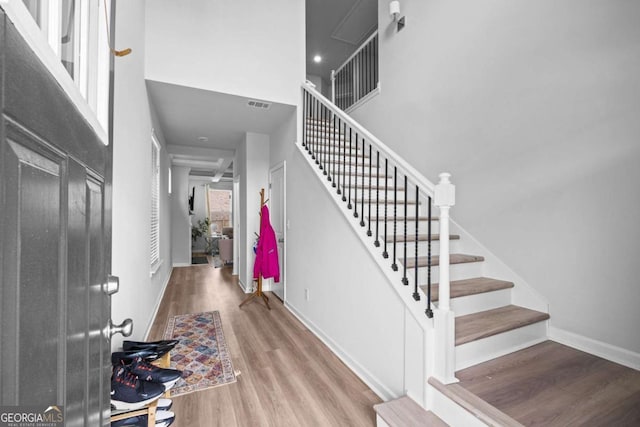 entryway featuring stairs, baseboards, wood finished floors, a towering ceiling, and visible vents